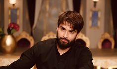 a man with a beard sitting at a table in front of a gold and black chair