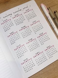 a calendar and two pens sitting on top of a desk next to a notebook with writing