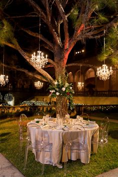 the table is set up for an outdoor dinner party with chandeliers hanging from the ceiling