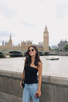 a woman standing on the side of a bridge next to a body of water with a clock tower in the background