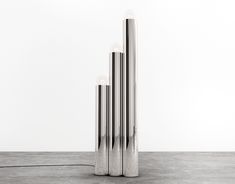 three metal tubes sitting on top of a floor next to each other in front of a white wall