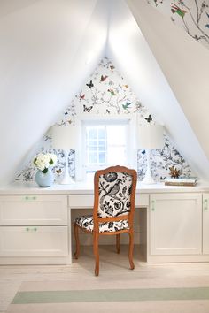 a chair sitting in front of a desk under a slanted ceiling with butterflies on it