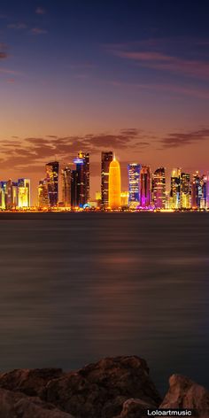 the city skyline is lit up at night with bright lights in the buildings and water