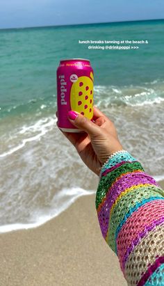 a person holding up a can of soda on the beach