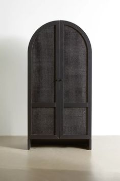 a black cabinet with an arched door on the top and bottom, in front of a white wall