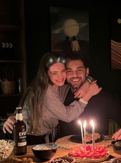 a man and woman are hugging in front of a cake with lit candles