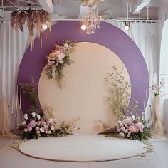 a wedding stage with flowers and chandelier hanging from it's ceiling in front of a purple backdrop