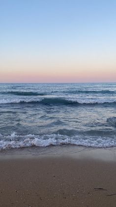 the ocean waves roll in and out onto the beach at sunset with pink hues