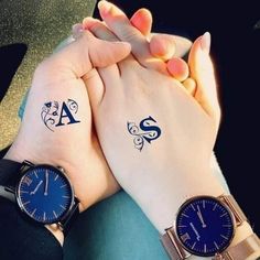 two people holding hands with tattoos on their wrists and one has a blue watch