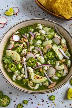 a bowl filled with vegetables and sauce next to tortilla chips on a table