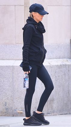 a woman in black jacket and leggings walking down the street with water bottle