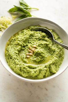 a white bowl filled with green pesto on top of a table next to a spoon