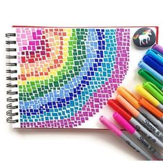 a notebook with markers and pens next to it on a white surface, which has a rainbow design in the middle