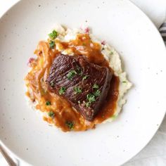 a white plate topped with meat and mashed potatoes covered in gravy next to a fork