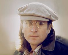 a man with long hair wearing glasses and a hat is looking at the camera while standing outside