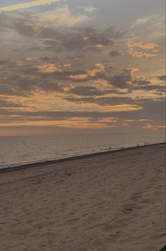 a person walking on the beach with a surfboard under an orange and blue sky