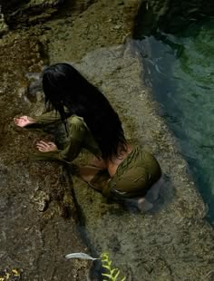 a woman is sitting on some rocks by the water