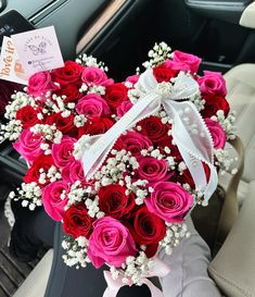 a heart - shaped arrangement of red and pink roses sits in the front seat of a car