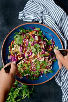 someone cutting up a salad on a blue plate with carrots and lettuce