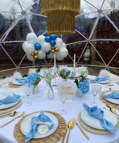 a table set with blue and white plates, napkins, silverware and balloons