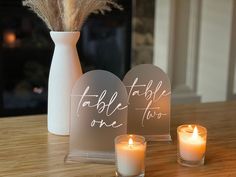 two candles are sitting next to each other on a table with a sign and vase