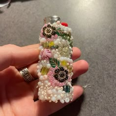 a hand holding a cell phone covered in beads and flowers