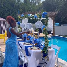 a woman in a blue dress standing next to a table set for a pool party