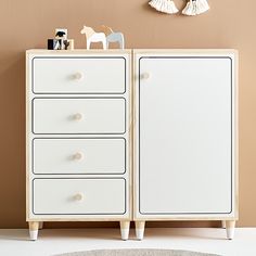 a white dresser with three drawers and two toy horses on top of it in front of a beige wall