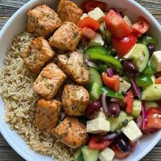 a white bowl filled with rice, meat and veggies next to a wooden table