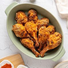 a green bowl filled with chicken wings next to bowls of seasoning