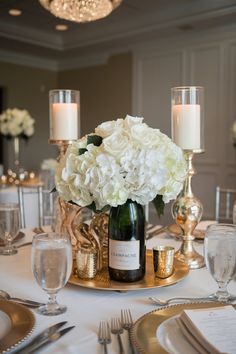 a table set with silverware and white flowers in a vase on top of a gold plate