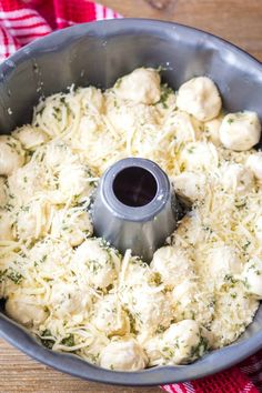 a pan filled with cheese and meatballs on top of a wooden table next to a red and white checkered towel