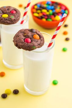 two glasses filled with milk and cookies on top of a yellow table next to candy