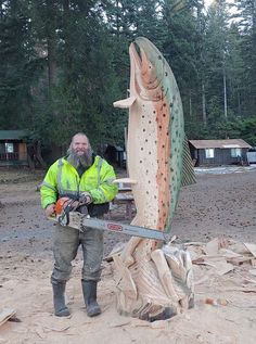 a man is holding a chainsaw next to a large fish statue in the woods