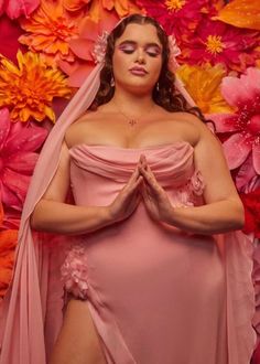 a woman in a pink dress and veil with flowers on the wall behind her is praying