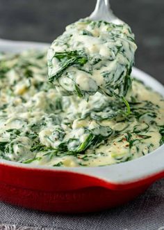 spinach dip in a red dish with a spoon scooping it up into the casserole