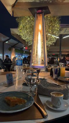 a table topped with plates and cups filled with food next to a tall light fixture