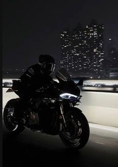 a man riding on the back of a motorcycle down a highway at night with city lights in the background