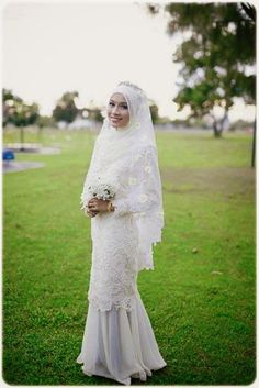 a woman in a white dress and veil posing for a photo on the grass with her bouquet