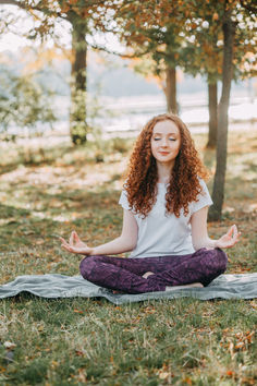 a woman is sitting in the grass doing yoga