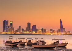 three boats are docked in the water near a city at sunset with skyscrapers in the background