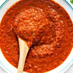 a white bowl filled with red sauce and a wooden spoon in the bowl next to it