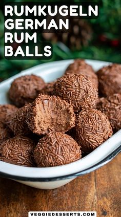 a white bowl filled with chocolate rum balls on top of a wooden table next to pine cones