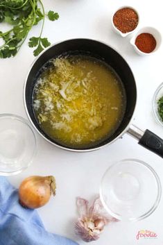 a pan filled with broth next to other ingredients on a white counter top, including onions and parmesan cheese