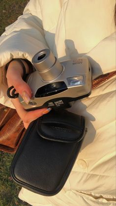 a person is holding a camera in their hand while sitting on the grass with other items