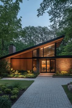 a modern house in the woods with brick walkway and large glass windows on each side