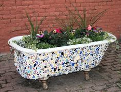 an old bathtub with flowers in it on the ground next to a brick wall