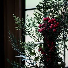 red berries and greenery in a vase on a table next to a window sill