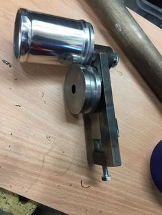 a metal object sitting on top of a wooden table next to a hammer and screwdriver