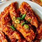 a white plate topped with chicken wings covered in sesame seeds and green onion flakes